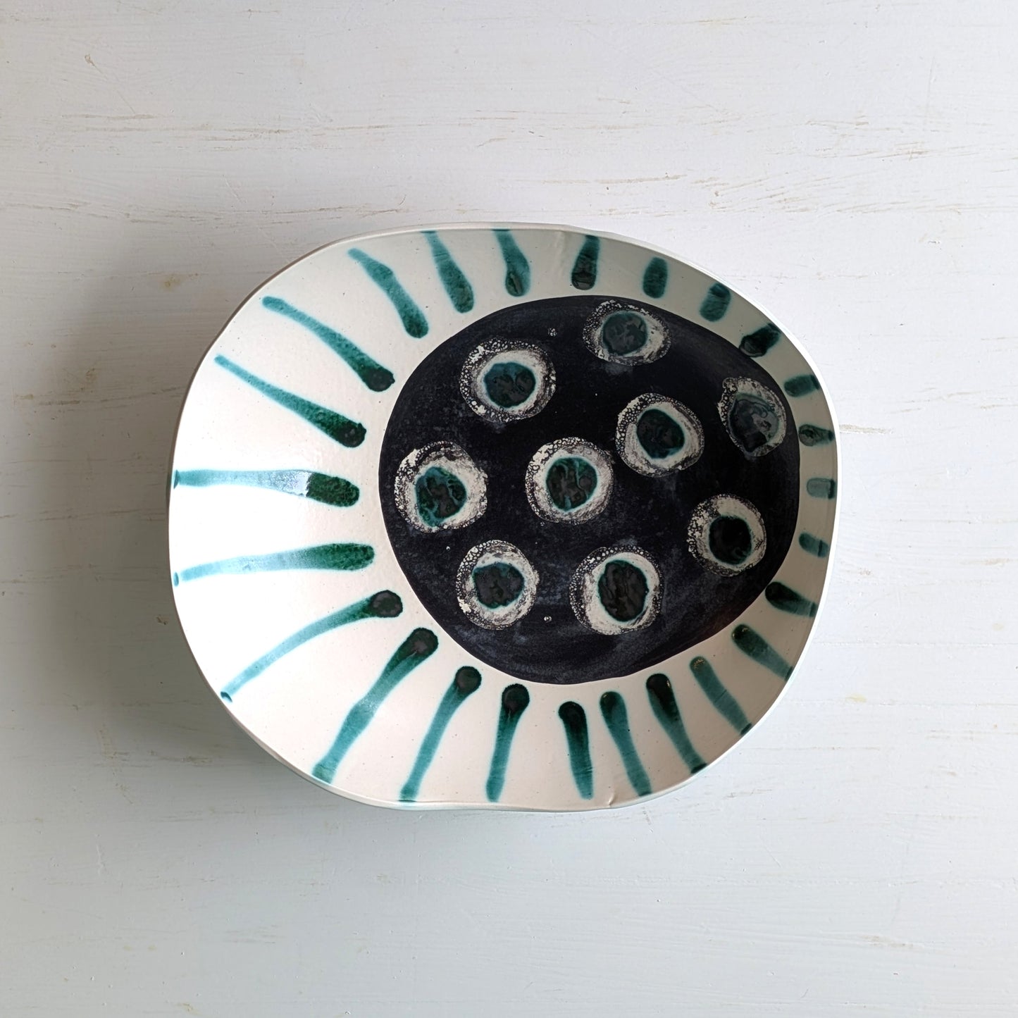 Top view of a white and green striped ceramic bowl with abstract design on a white table