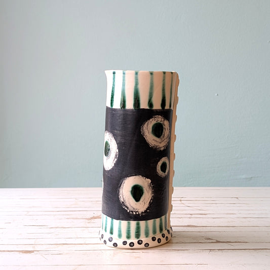 Ceramic vase with black, white, and green patterns on a light wooden surface and gray background