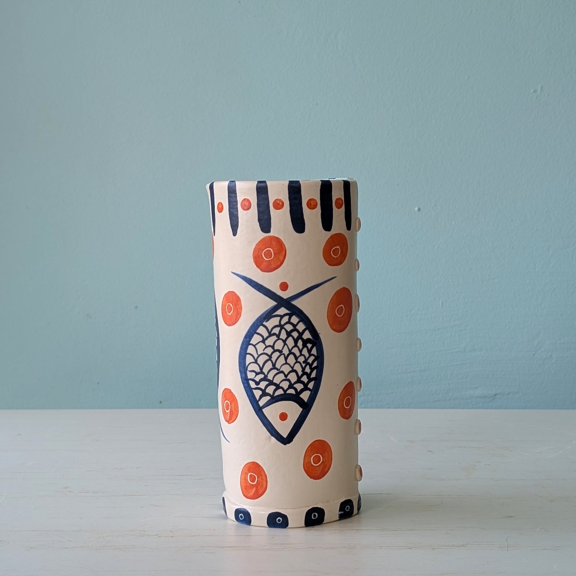 Cylindrical ceramic vase with fish design and orange circles on a light blue background