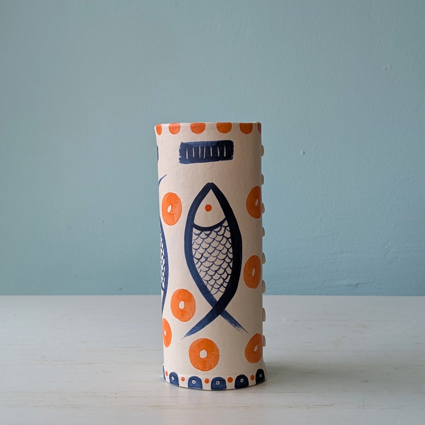 Cylindrical ceramic vase with fish and orange circle design on a light blue background