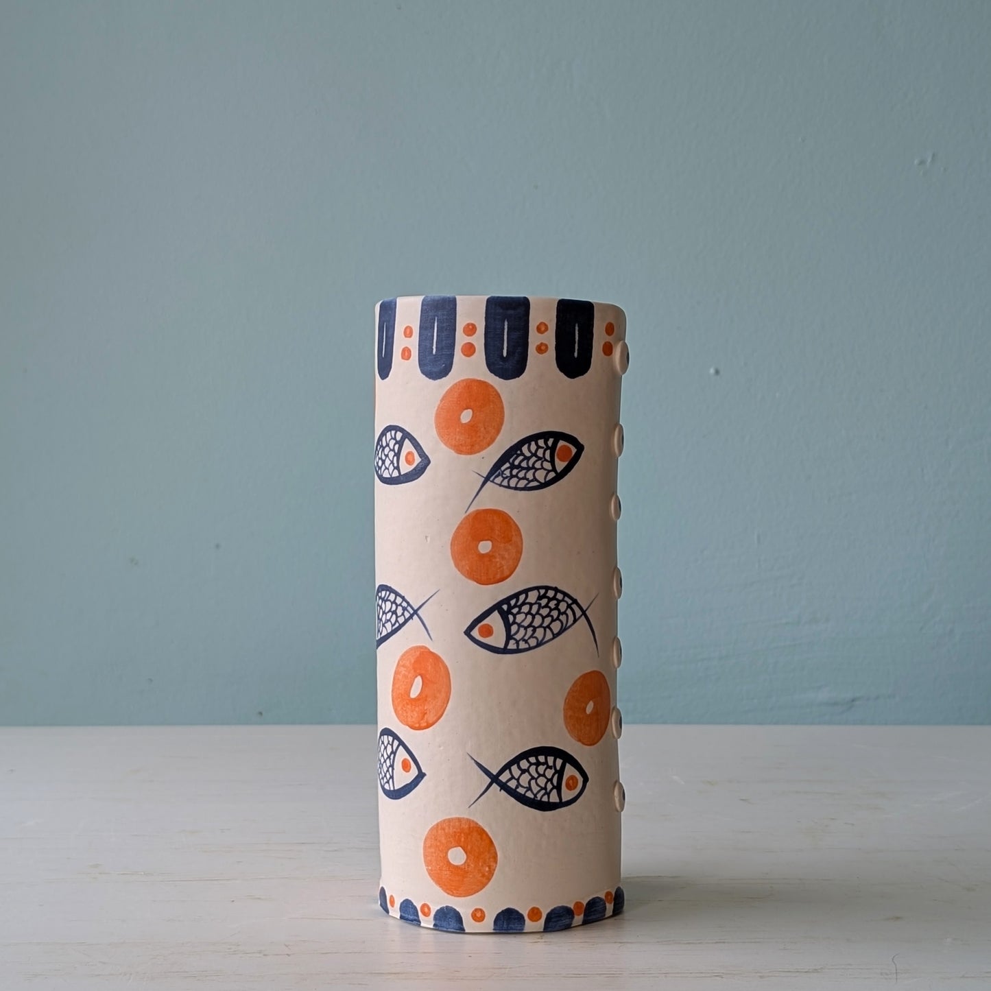 White ceramic pourer with blue fish and orange circle pattern on a white table against a blue wall