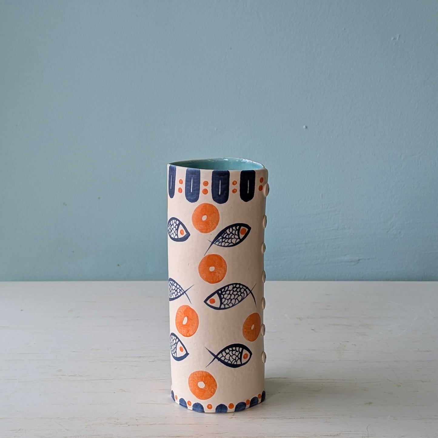 Cylindrical ceramic pourer with fish pattern on a light blue background