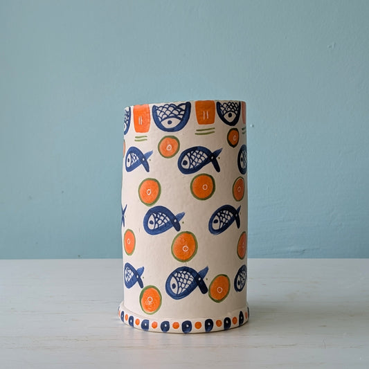 White ceramic vase with blue fish and orange circle pattern on a white table against a blue wall