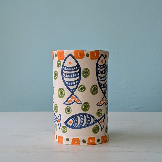 Cylindrical ceramic vase with fish and dot pattern on a light blue background