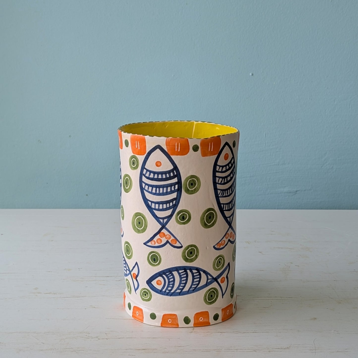 Decorative cylindrical vase with fish pattern on a light blue background