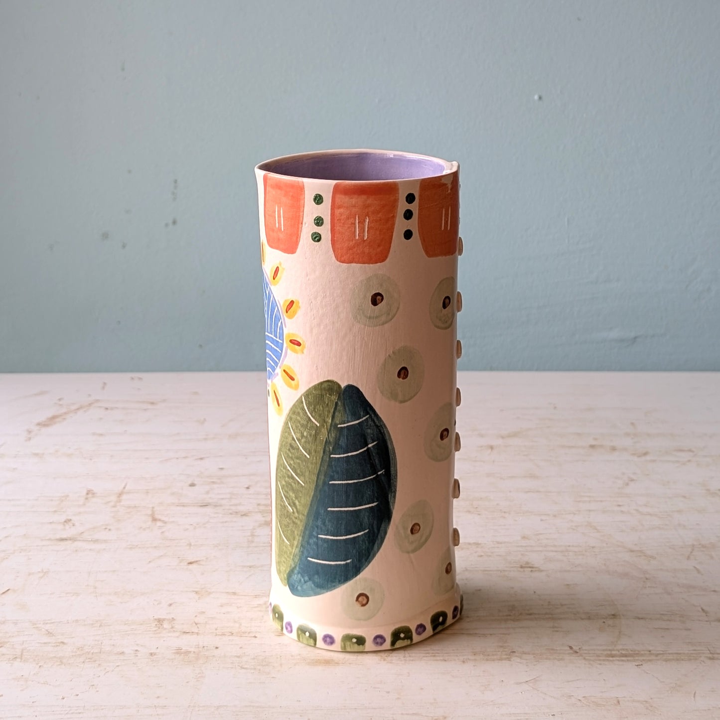 Cylindrical ceramic vase with colorful patterns on a wooden surface and light blue background