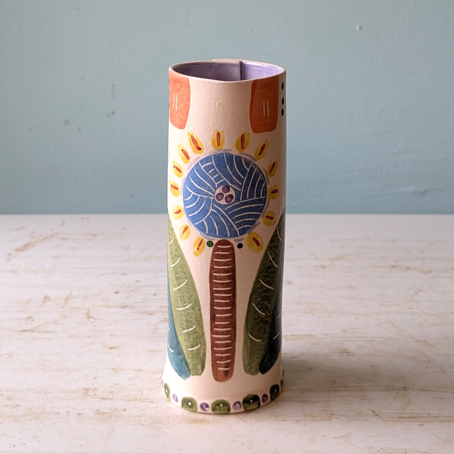 Ceramic vase with colorful patterns on a light wooden surface and light blue background