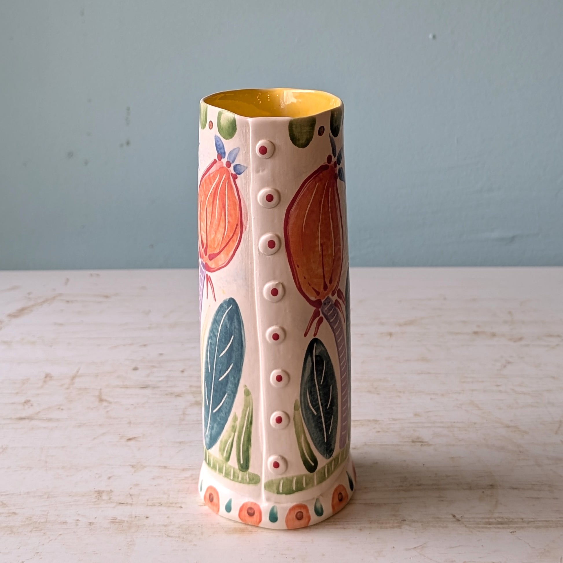 Decorative vase with fruit and leaf patterns on a light surface with a blue background