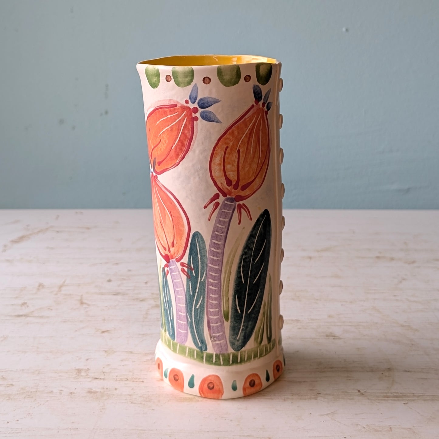 Decorative ceramic vase with floral patterns on a wooden surface and light blue background