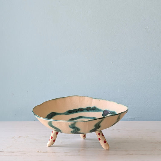 Beige ceramic bowl with legs and green spiral pattern