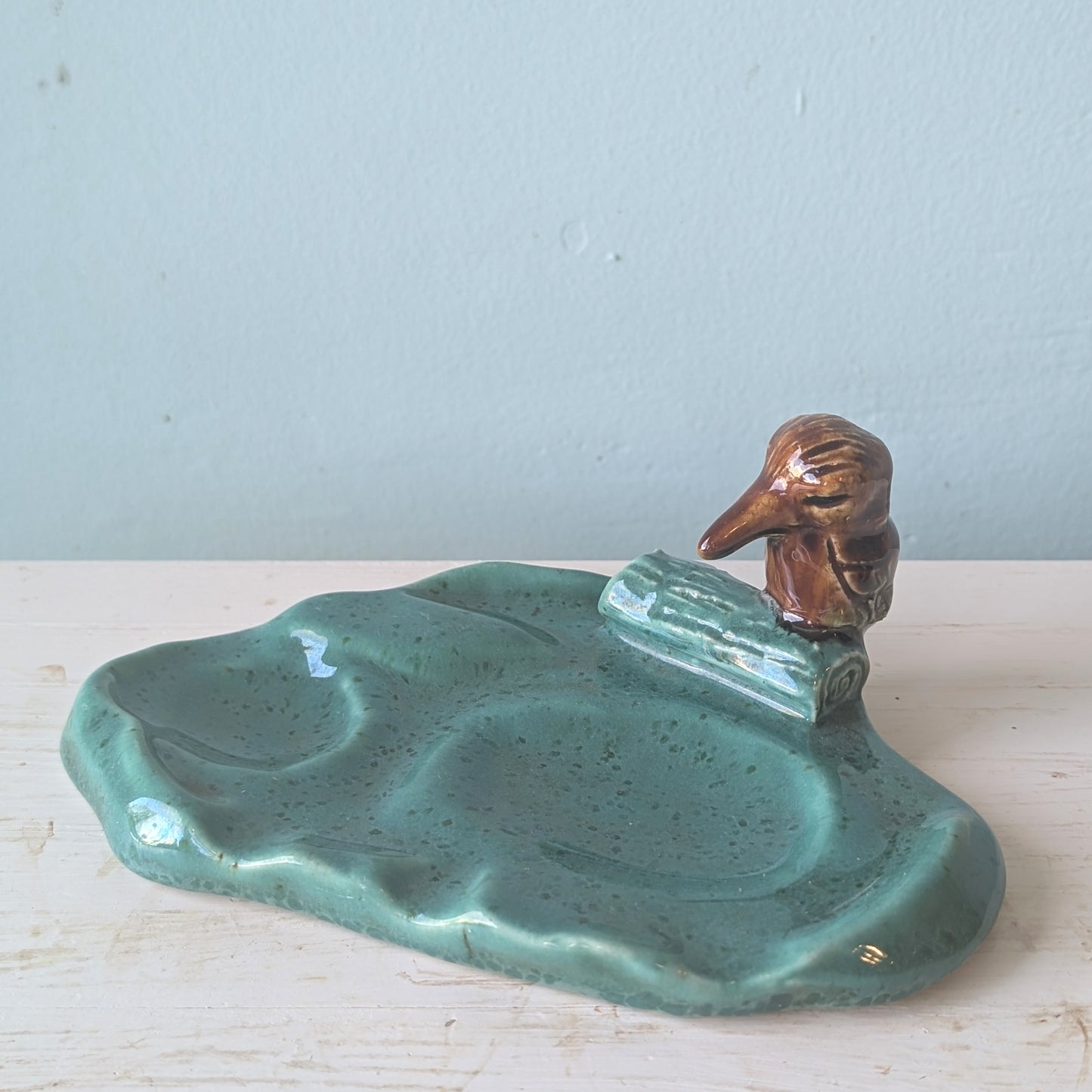 Ceramic kookaburra plate with a green body and brown bird figurine on a light blue background