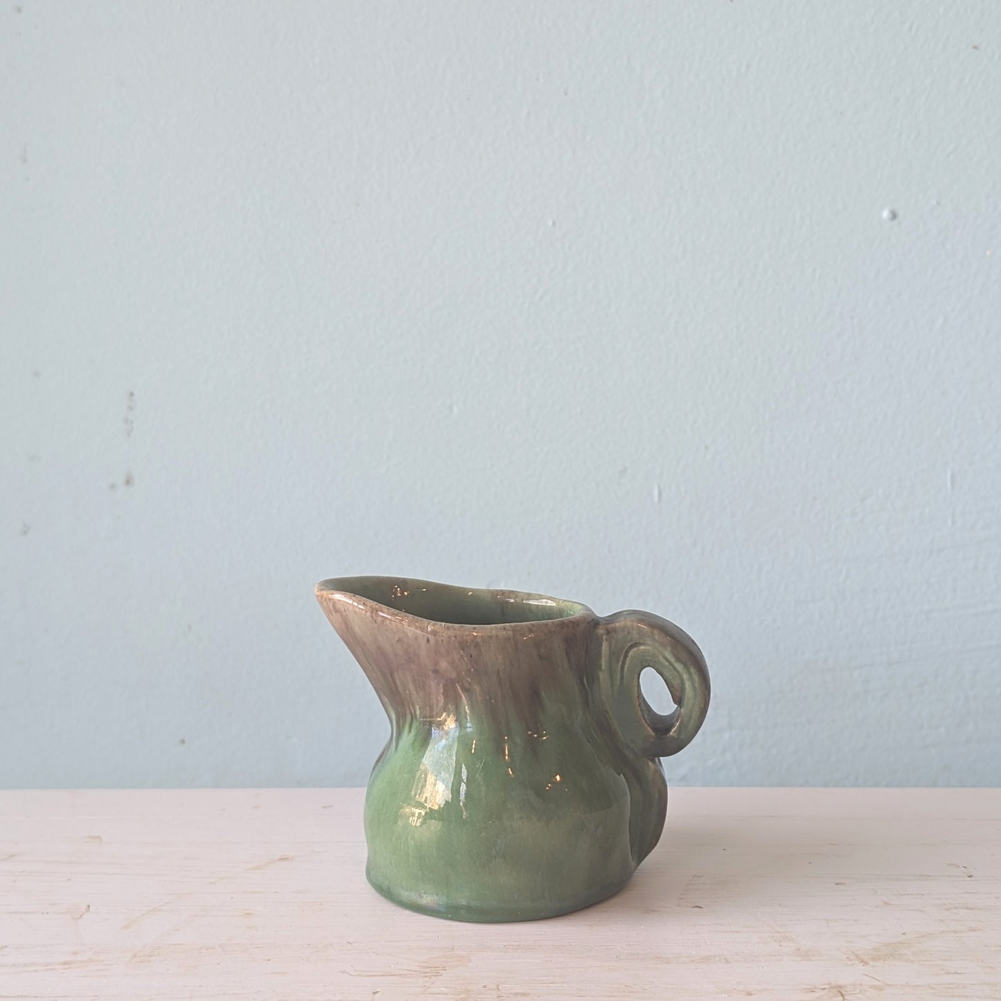 Green ceramic milk jug on a light wooden surface with a light blue background