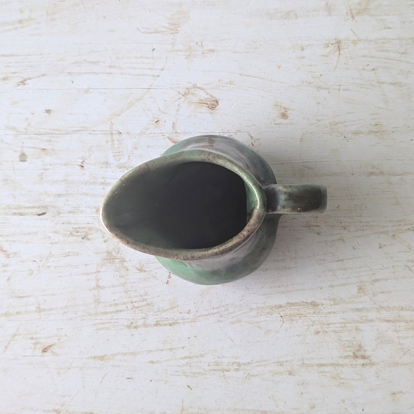 Green ceramic milk jug on a textured white surface