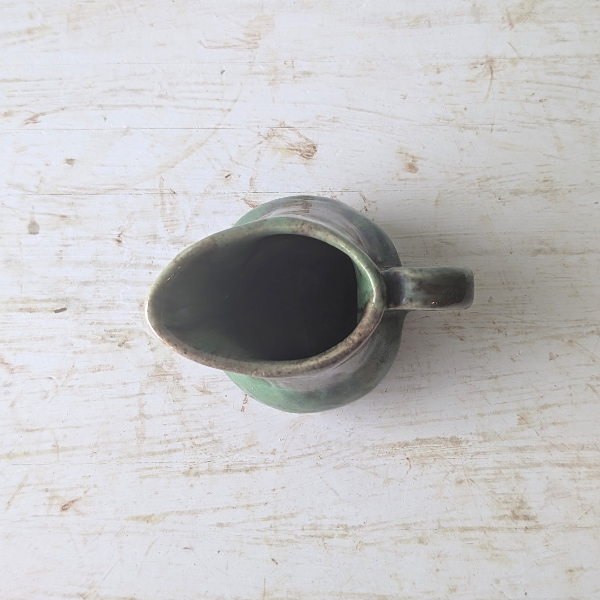 Green ceramic milk jug on a textured white surface