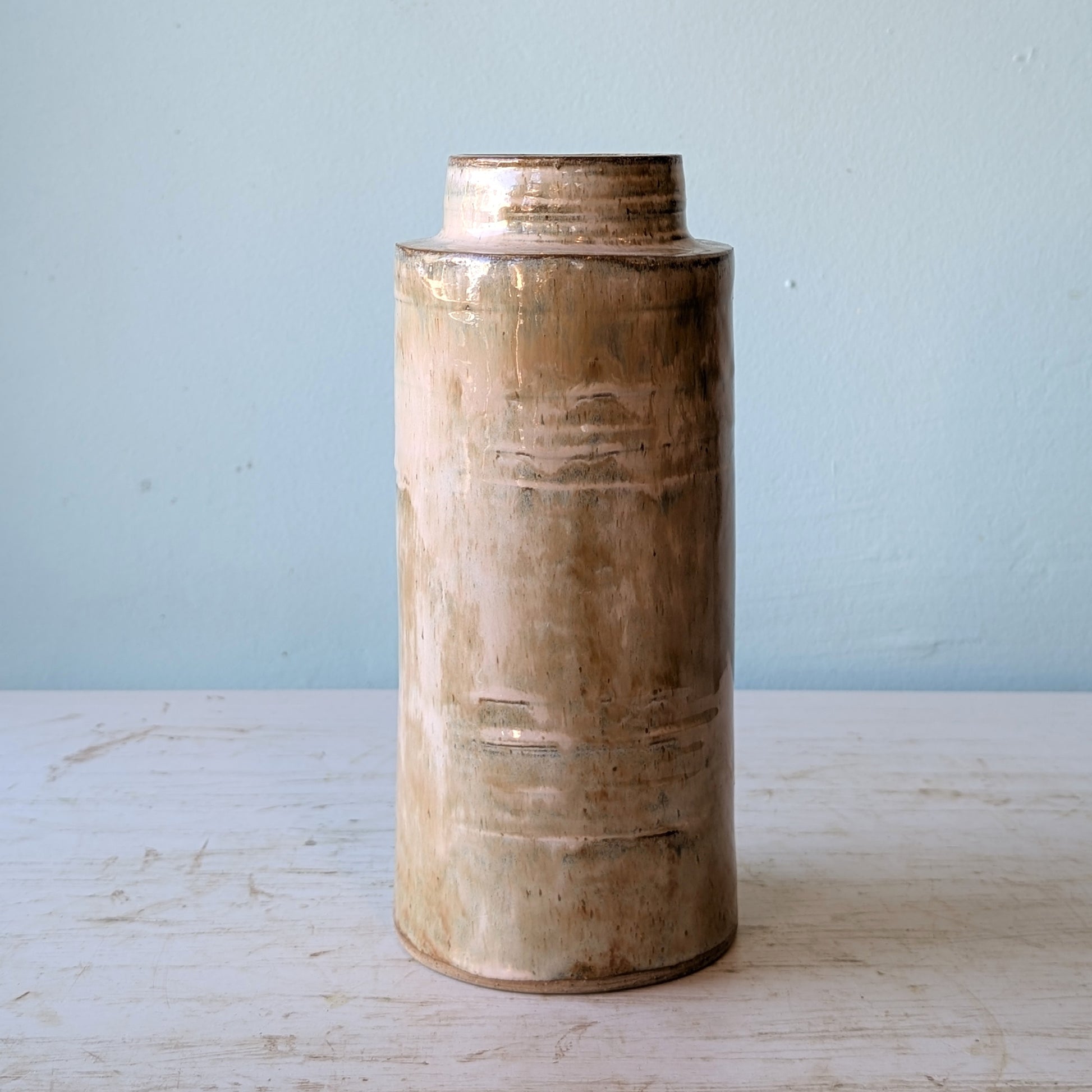 Cylindrical ceramic vase with textured surface on a light wooden surface against a light blue wall.