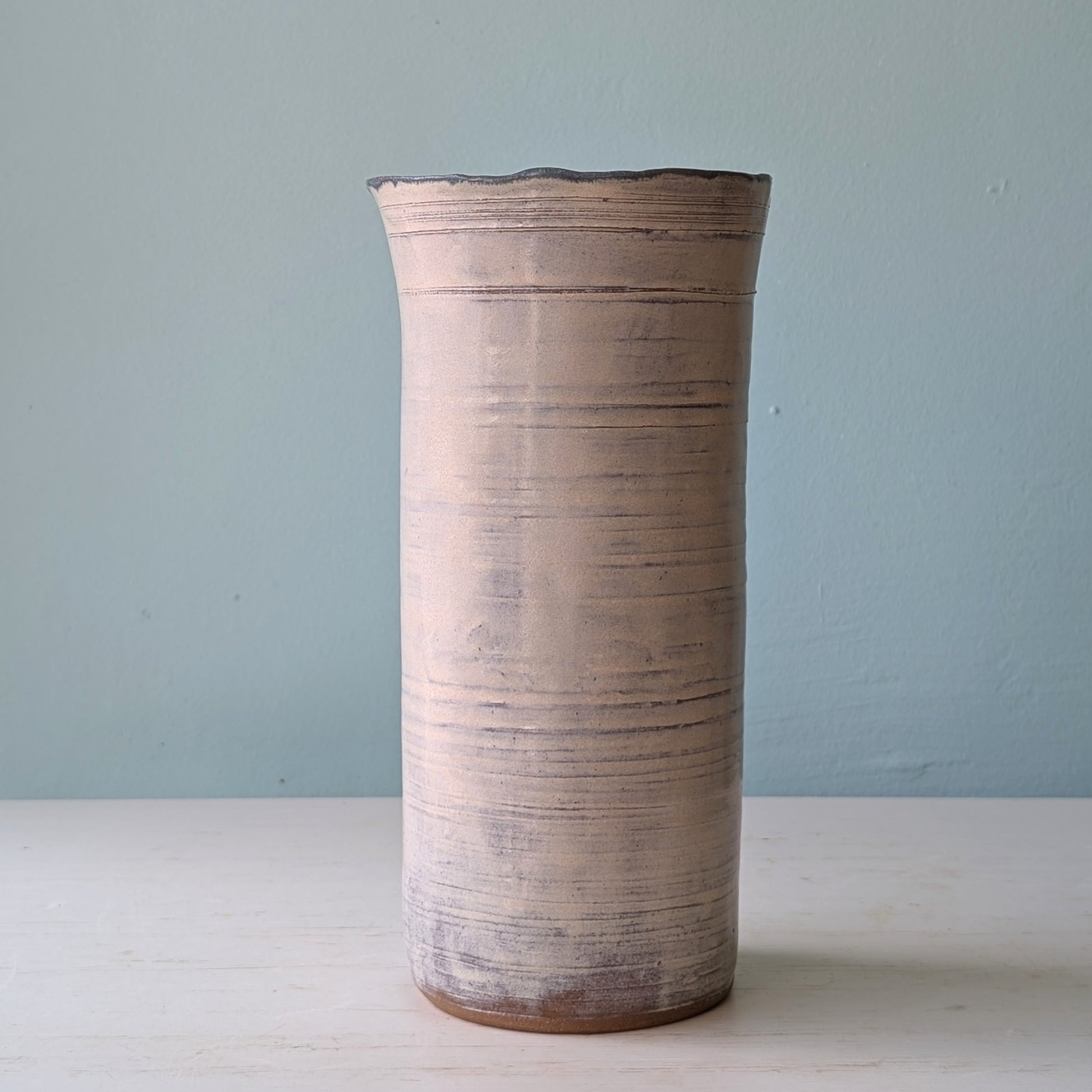 Cylindrical ceramic vase with textured surface on a light blue background