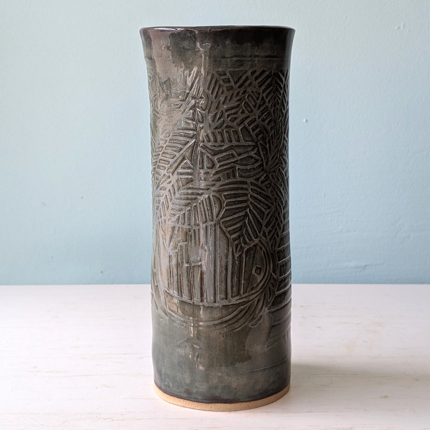 Cylindrical ceramic vase with textured design on a light blue background
