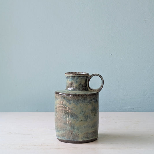 Green ceramic jug on a white table against a blue wall