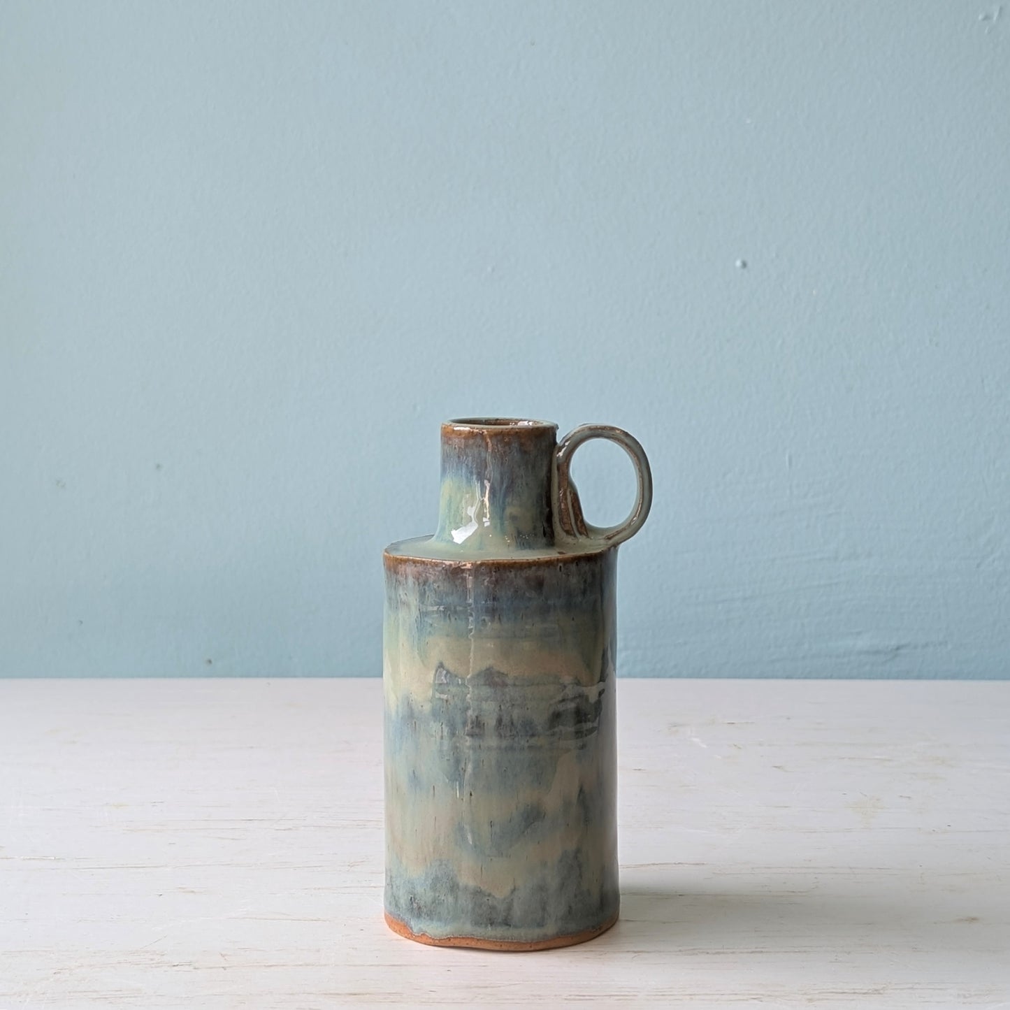 Green ceramic jug with handle on white table against a blue wall