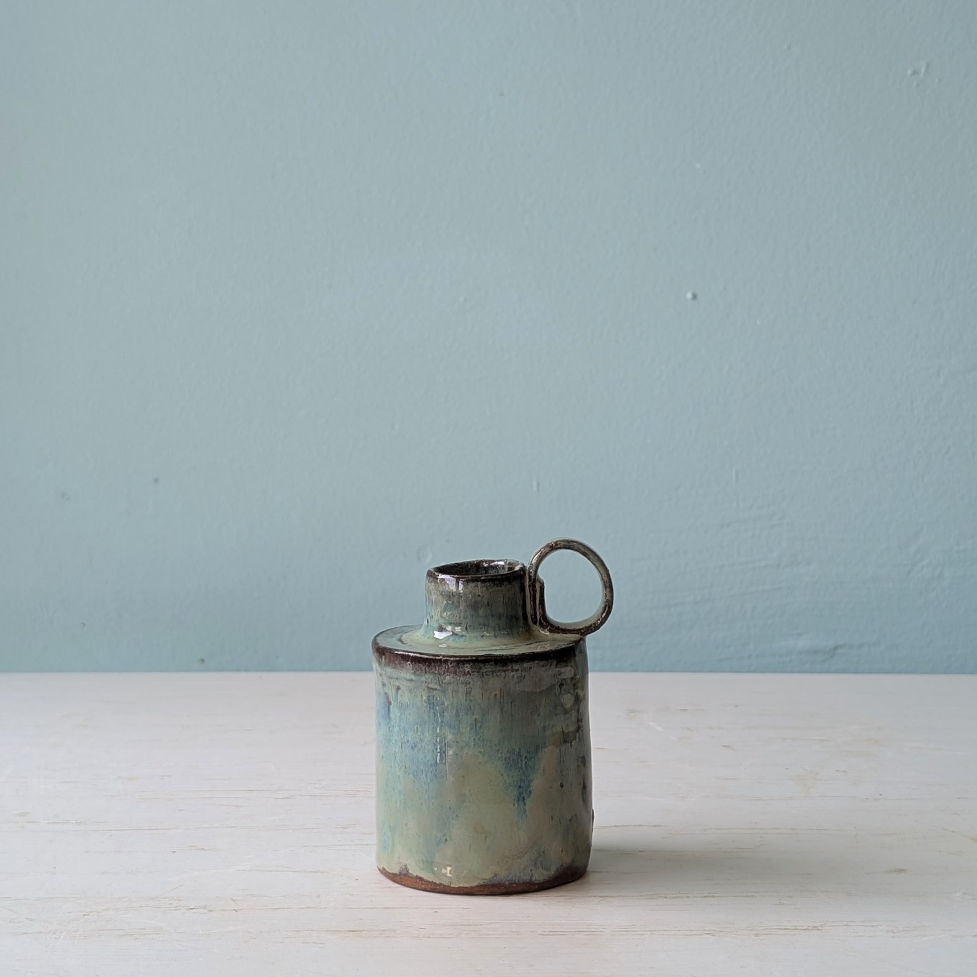 Ceramic jug with a handle on a white surface against a light blue wall