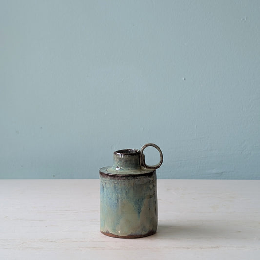 Ceramic jug with a handle on a white surface against a light blue wall