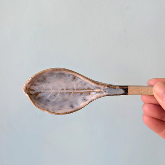 Ceramic spoon with leaf pattern against a light blue background