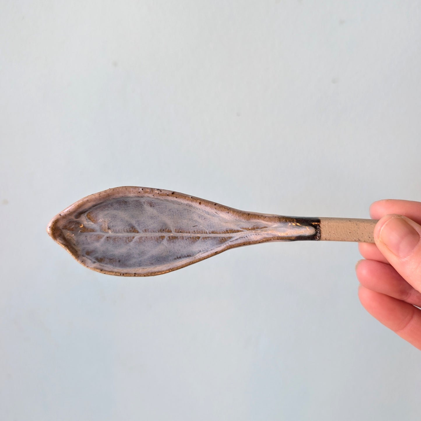 Person holding a ceramics spoon on a light blue background