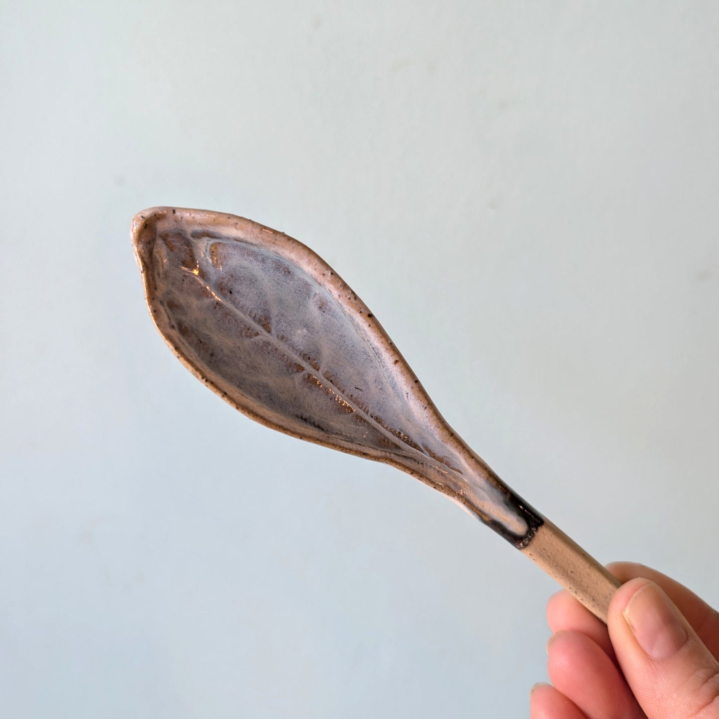 Hand holding a ceramic spoon against a light blue background