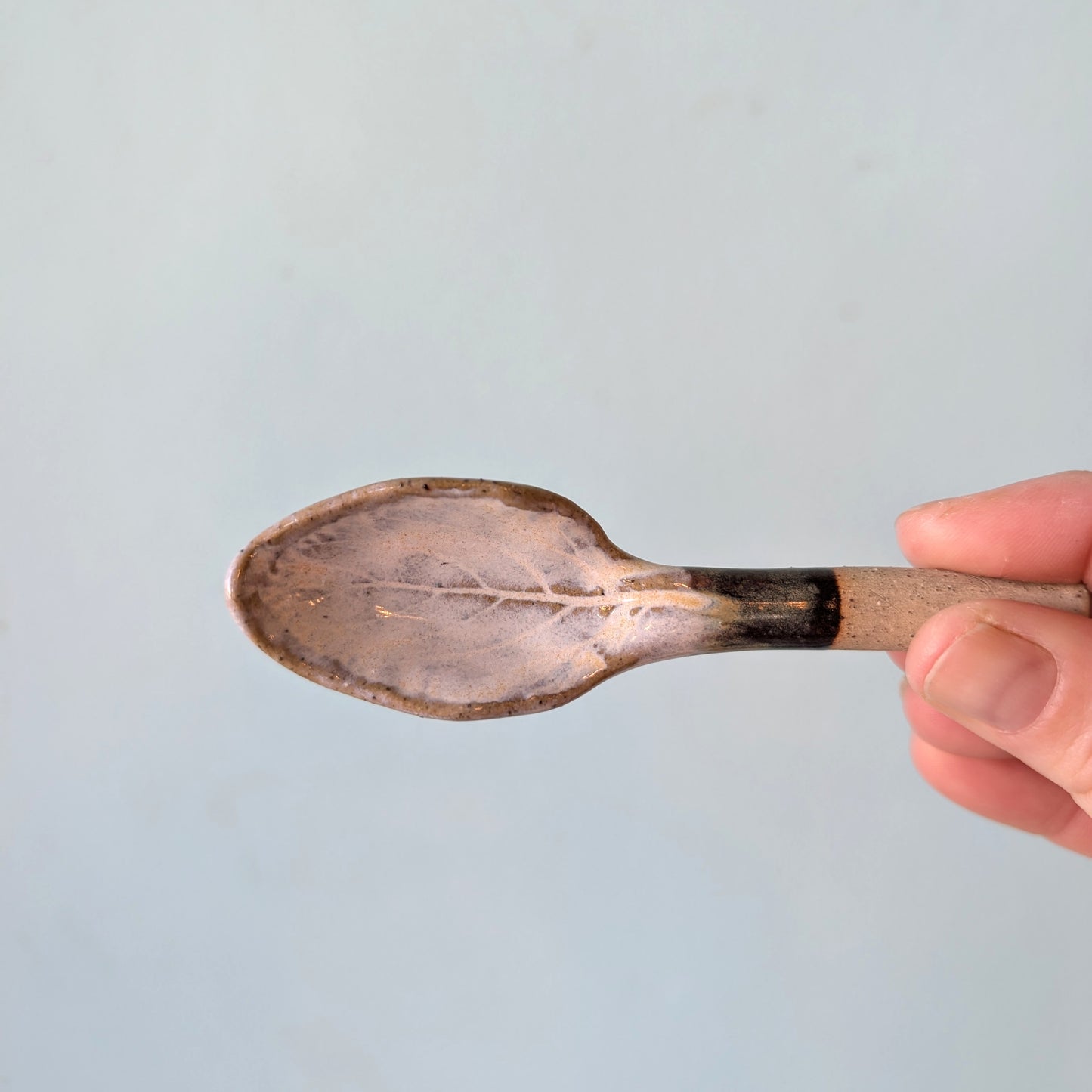 Ceramic spoon held by a hand against a light blue background