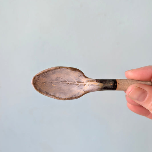 Ceramic spoon held by a hand against a light blue background