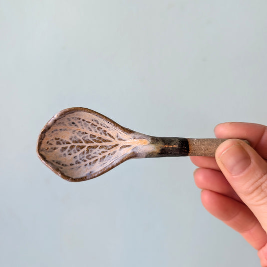 Hand holding a ceramic spoon against a light blue background