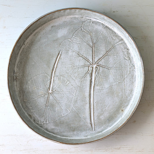 Ceramic bowl with leaf patterns on a light wooden surface