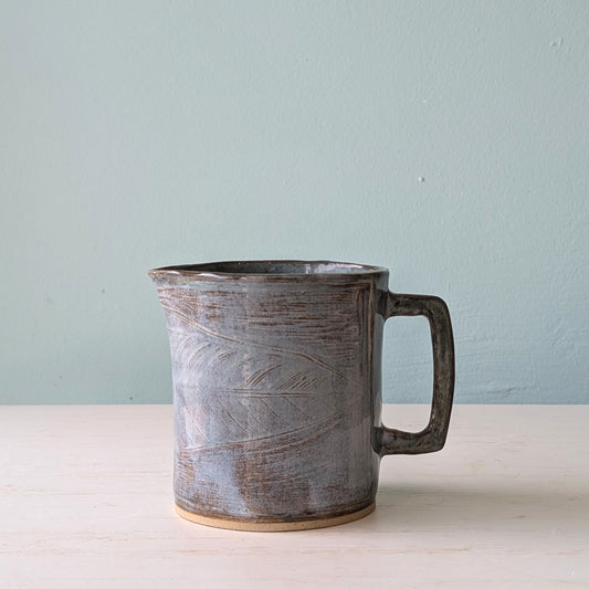 Ceramic jug with a handle on a light surface against a light blue wall