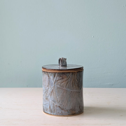 Textured ceramic cannister with lid against blue background