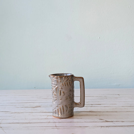 Front view of a small ceramic milk jug with linocut flower pattern