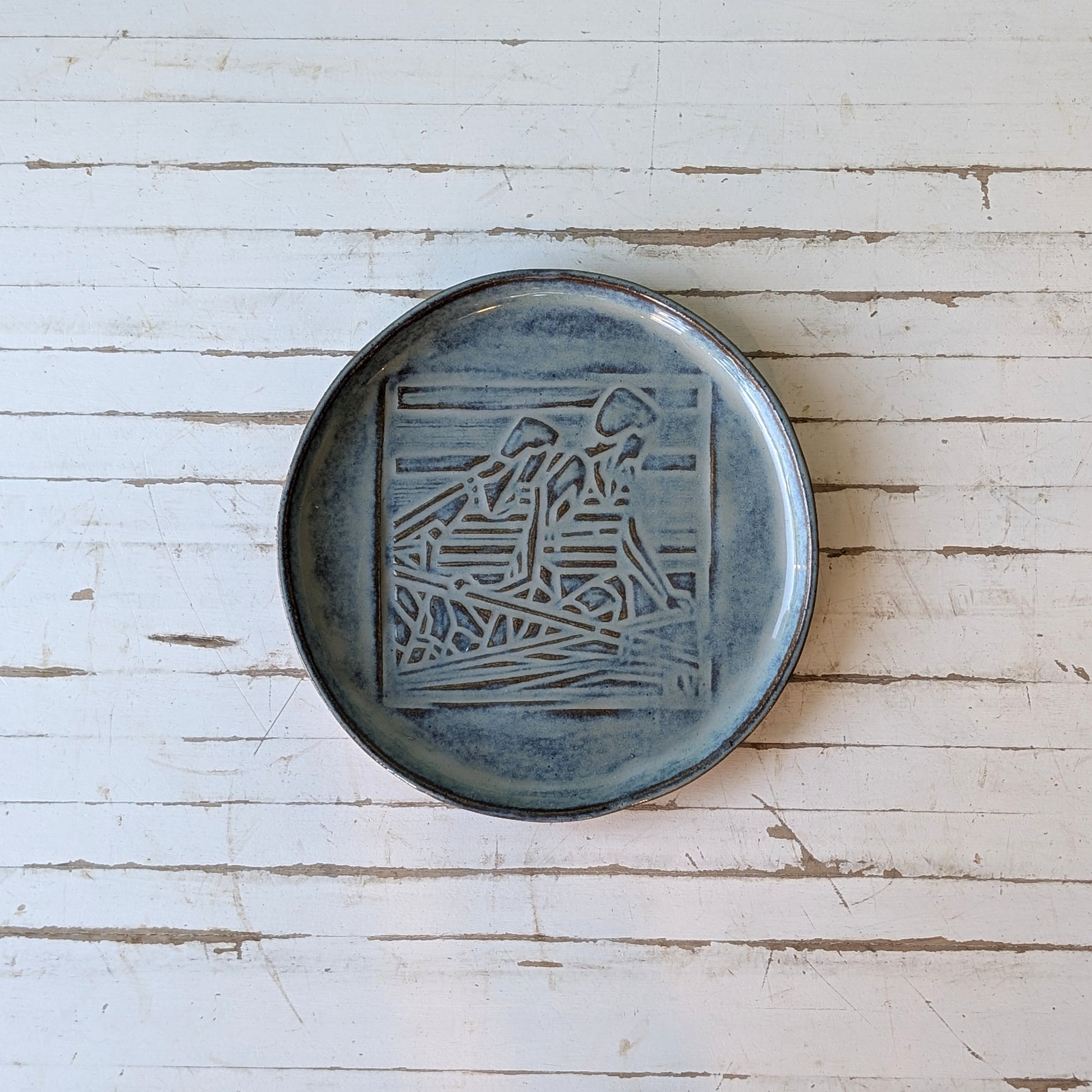 Top view of a blue ceramic serving platter with linocut pattern of two rowers