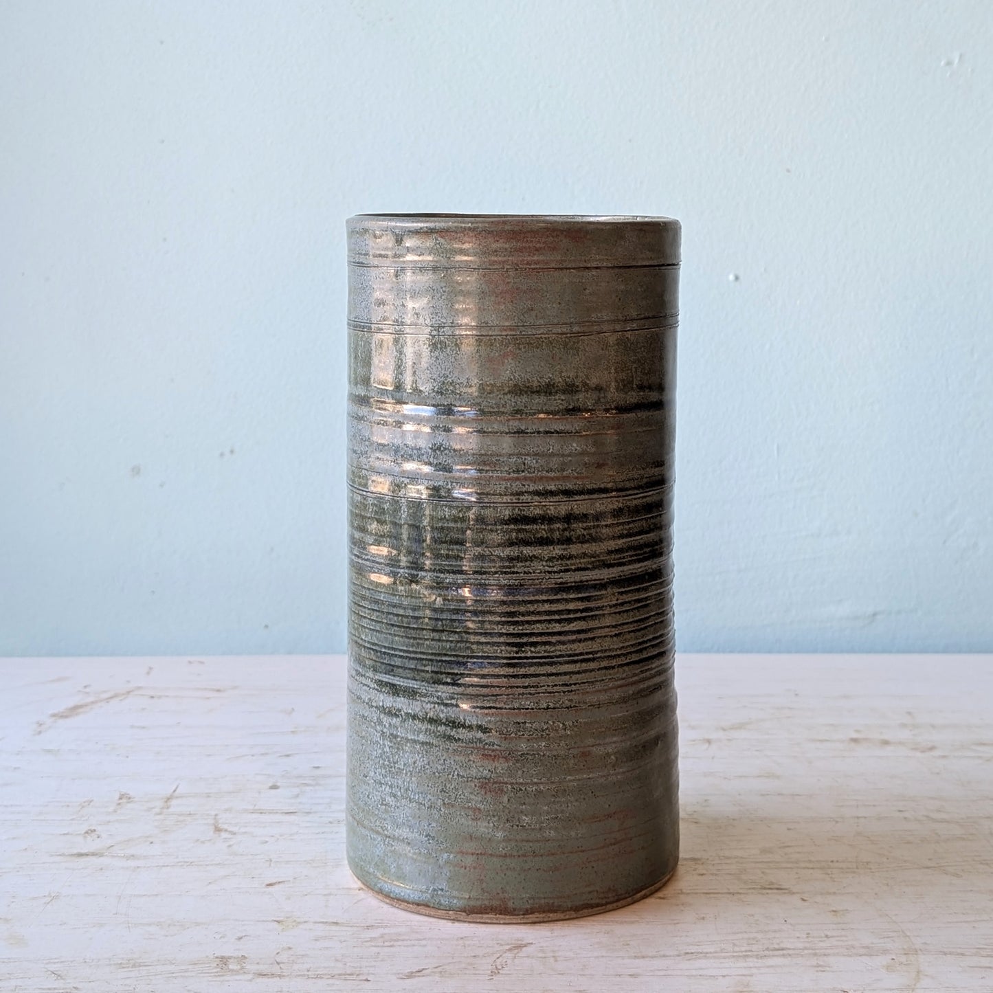 Cylindrical ceramic vase with textured surface on a light wooden surface and light blue background