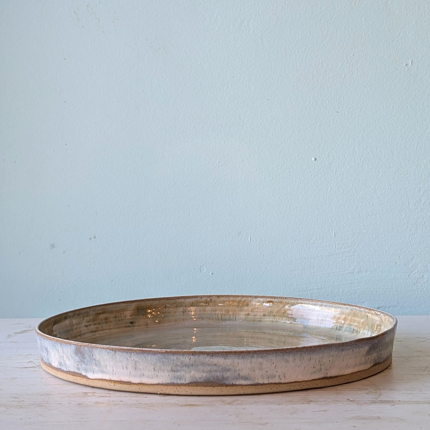 Round ceramic platter on a light wooden surface with a light blue wall background