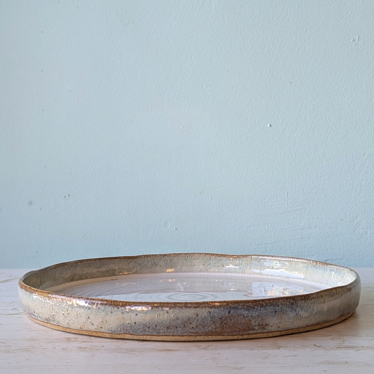 Round ceramic platter with a textured edge on a light wooden surface against a light blue wall.