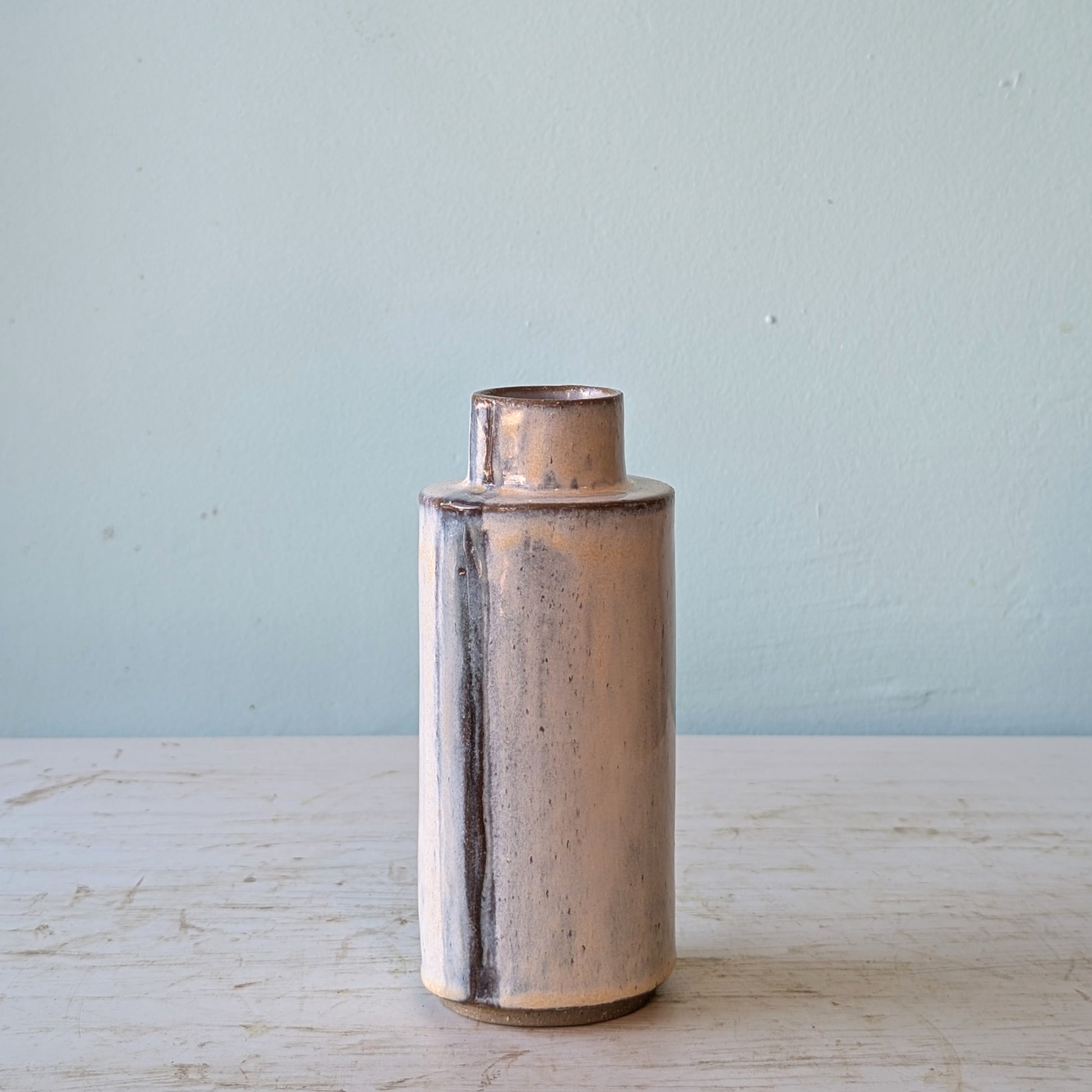 Cylindrical ceramic vase on a light wooden surface and light blue background