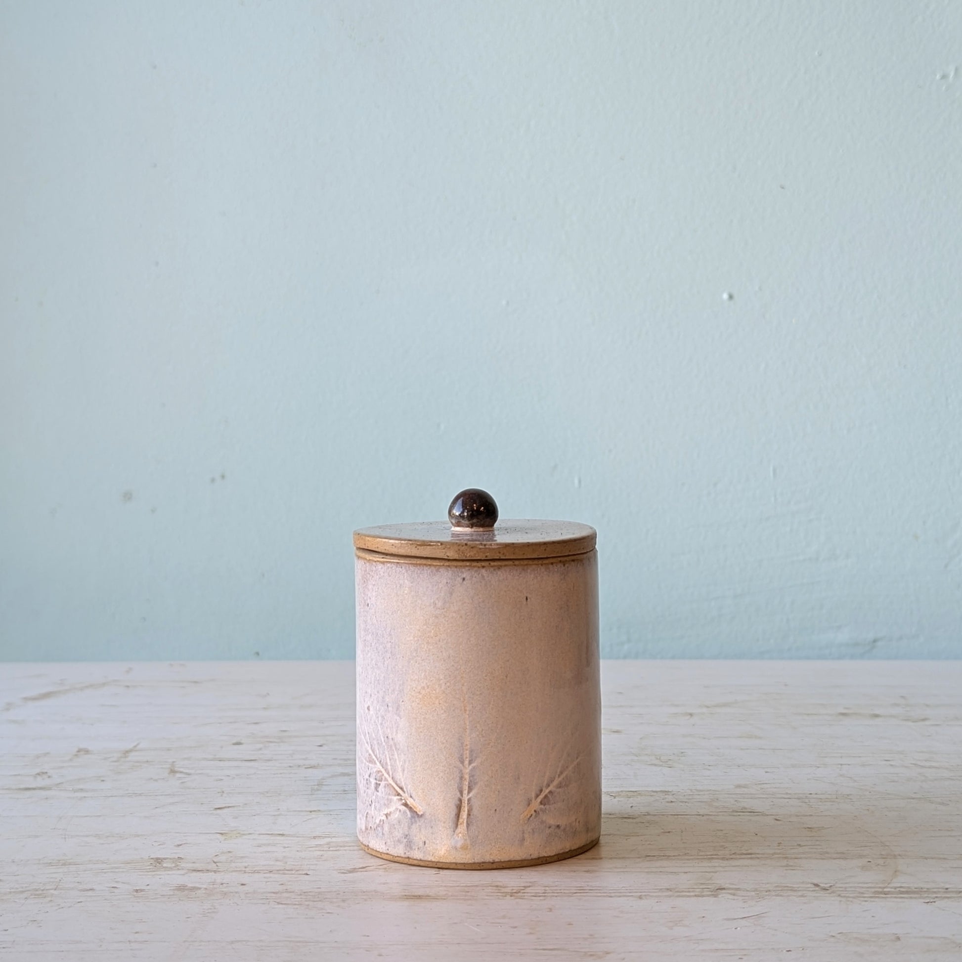 Ceramic jar with a lid on a light wooden surface with a light blue background