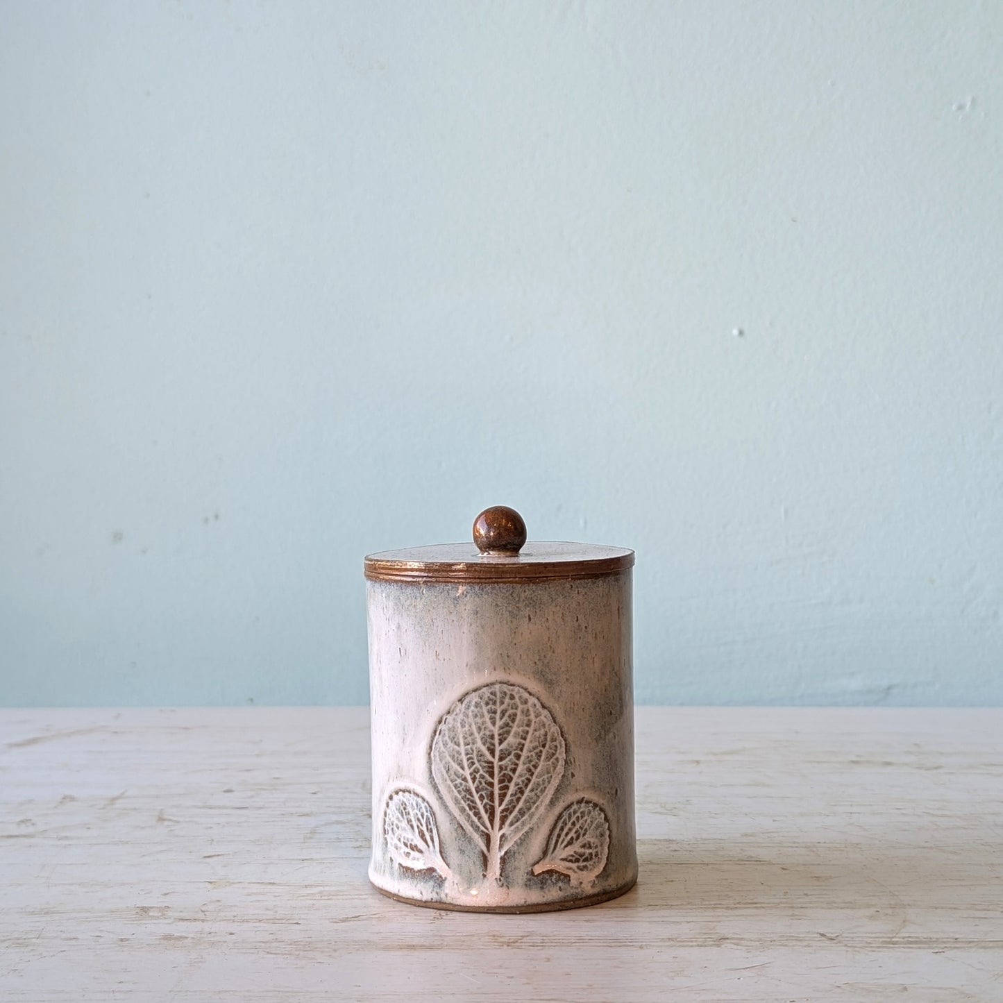 Ceramic jar with decorative lid on a wooden surface with a light blue background