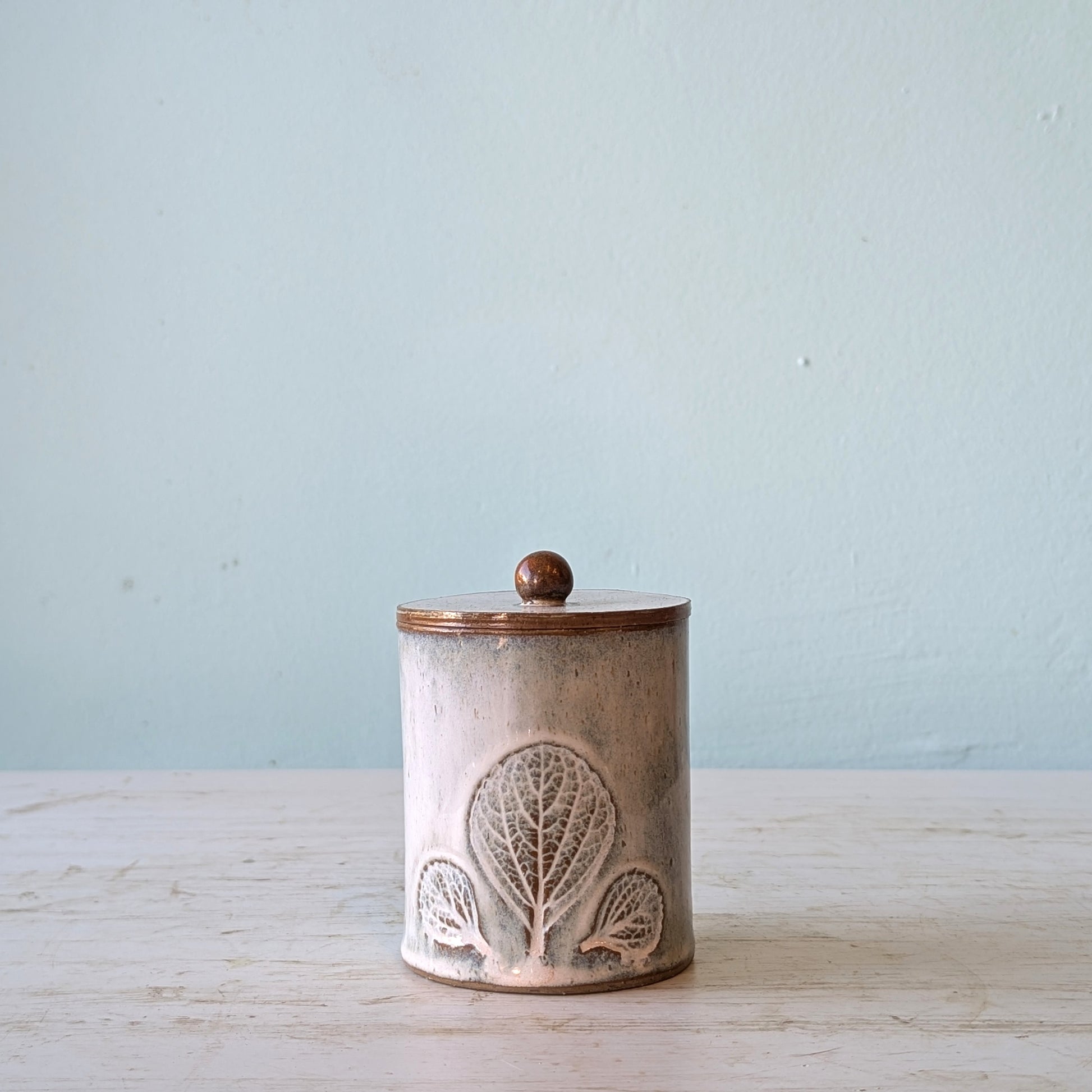 Ceramic jar with decorative lid on a wooden surface with a light blue background