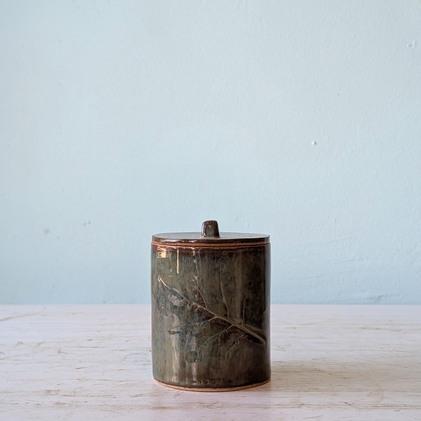 Ceramic jar with a textured surface on a light wooden surface with a light blue background