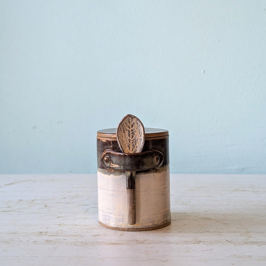 Ceramic jar with ceramics lid and attached spoon on a light wooden surface and blue background