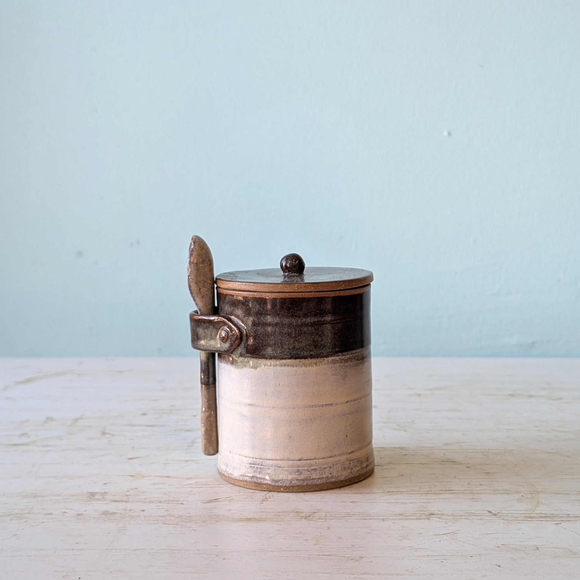 Ceramic canister with a lid and handle on a light wooden surface with a light blue background