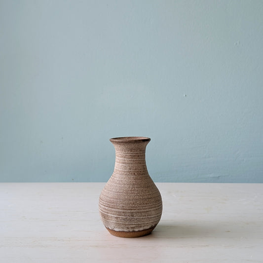 Small brown ceramic bud vase on white table against a blue wall