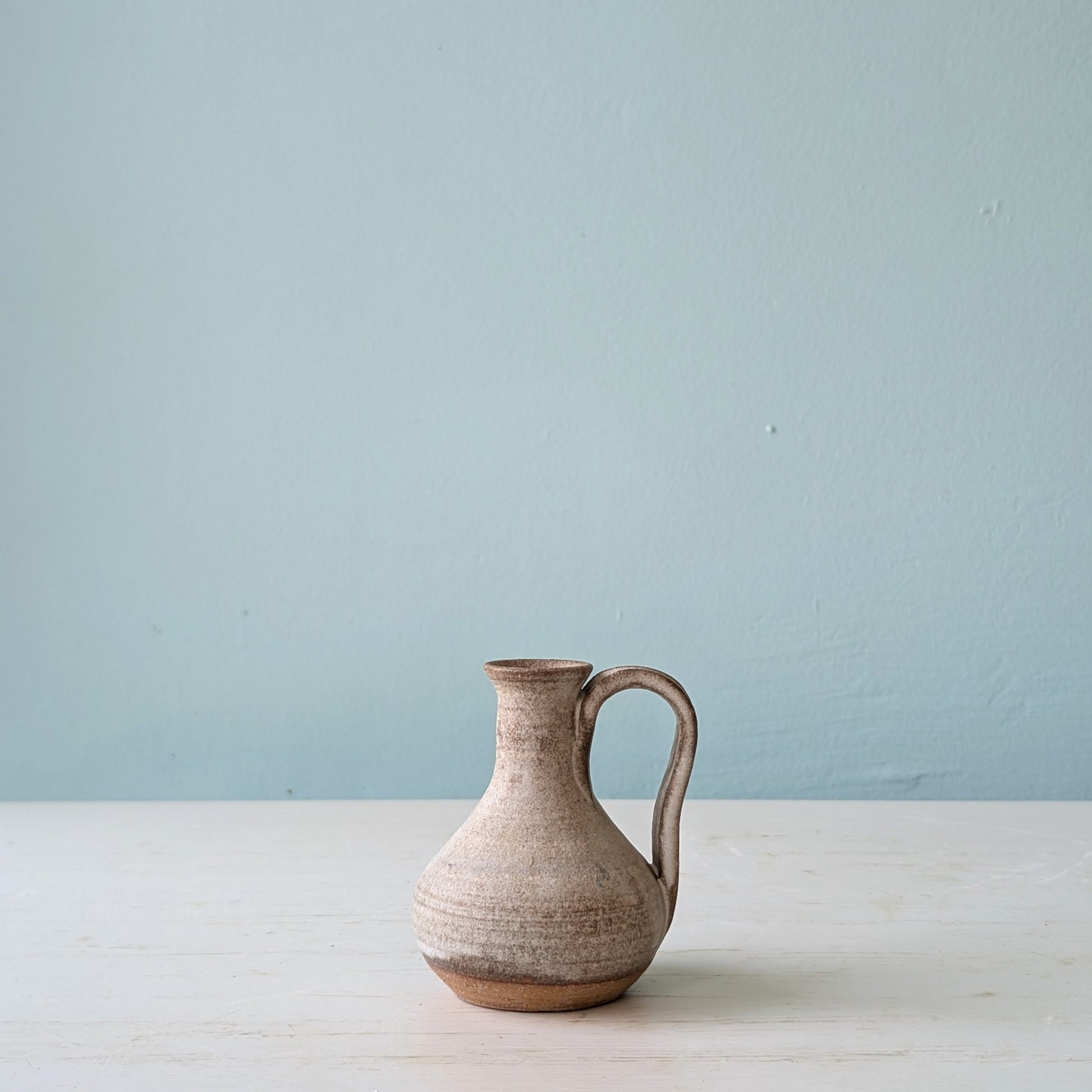Ceramic pitcher on a white surface with a light blue background