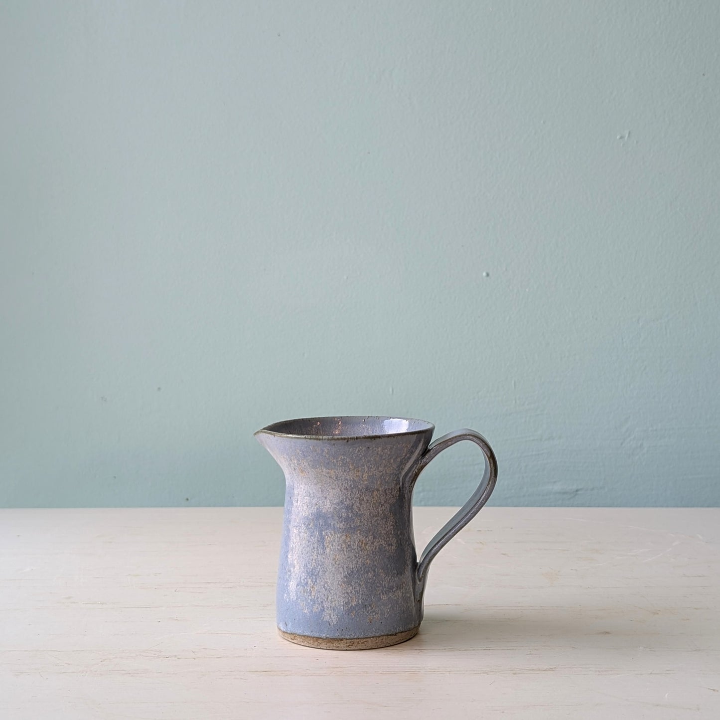 Small blue milk jug on a white table against a blue wall