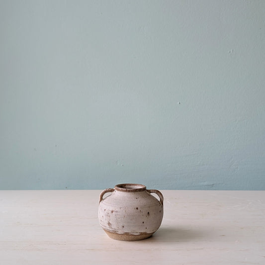 Small vase with two handles on a white table against a blue wall